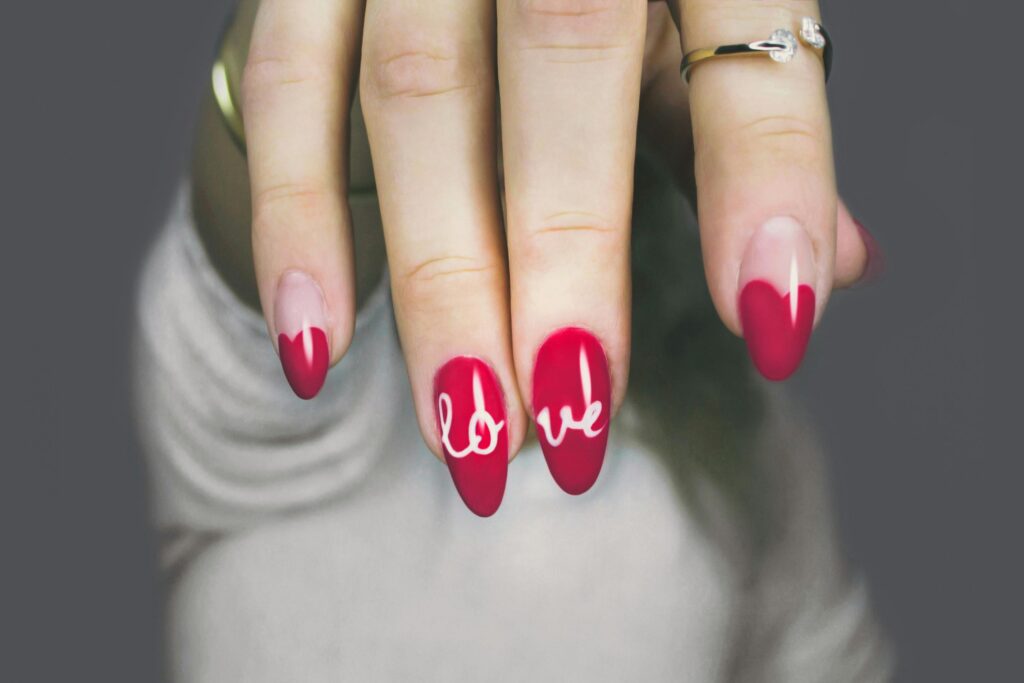 pexels-photo-887352-887352 Vibrant red nails with 'love' art on a woman's hand, showcasing elegant style and design.